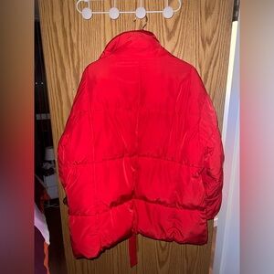 Red puffer jacket with a belt, snaps, and a high collar. The jacket is quilted.